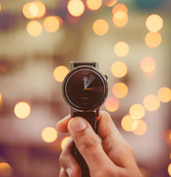 A hand holding a watch against warm out-of-focus lights.